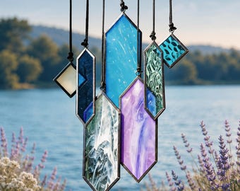 May include: A hanging mobile featuring seven geometric stained glass pieces in various shapes and sizes. The glass panels display shades of blue, purple, white, and green with marbled textures, all encased in dark metal frames and suspended by black cords.