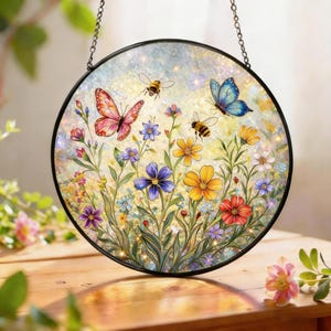 May include: Round stained glass panel featuring a vibrant garden scene. The design includes colorful flowers, butterflies, and bees. The panel is framed in black and hangs from a chain, perfect for window or wall decor.