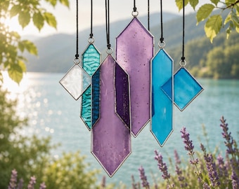 May include: A collection of seven geometric stained glass ornaments hanging from black cords. The pieces feature various shapes including elongated hexagons and diamonds in shades of translucent purple, deep violet, teal, and clear glass with metal edges.