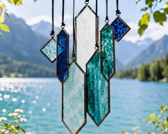 May include: A hanging mobile composed of multiple geometric stained glass pieces in shades of blue, teal, and white. The pieces are suspended by black cords and feature hexagonal and diamond shapes with textured, translucent glass surfaces.