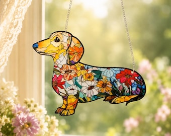 May include: A stained glass suncatcher shaped like a dachshund dog, featuring a vibrant mosaic pattern of multi-colored flowers in shades of red, orange, yellow, and blue. The piece is suspended by two thin silver metal chains for hanging.