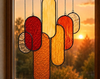 May include: A hanging suncatcher composed of multiple vertical oval-shaped stained glass panels in shades of red, orange, yellow, and clear textured glass. Each panel is framed in black metal and suspended by thin black chains at varying heights.