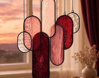 May include: A hanging mobile composed of multiple oval-shaped stained glass panels in varying shades of red, pink, and clear textured glass. Each panel is framed in a thin black metal border and suspended by individual black metal chains.