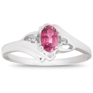 May include: A silver ring featuring a large, oval-cut pink gemstone as the centerpiece. Two smaller, round, clear gemstones flank the main stone. The ring has a simple, elegant design, with a smooth, polished band.