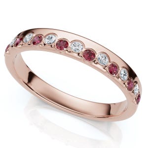May include: Rose gold ring featuring alternating round red gemstones and clear, sparkling stones. The ring's band is a polished rose gold, and the gemstones are set in a channel setting. A delicate and elegant piece of jewelry.