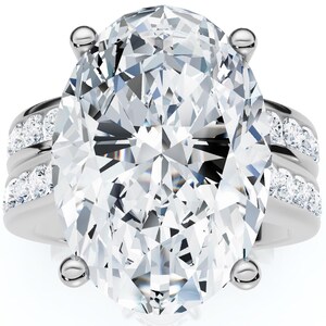 Puede incluir: Un anillo de tono plateado con una gran piedra central transparente de corte ovalado sujeta por cuatro garras. La banda se divide en dos filas paralelas a cada lado, cada una engastada con una serie de pequeñas piedras redondas y claras.