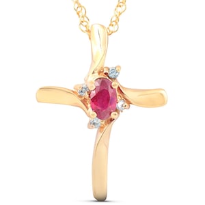 May include: A gold-colored pendant necklace featuring a cross design. The cross has a central oval-shaped ruby gemstone and is accented with small, round, clear gemstones. The necklace chain is also gold-colored.
