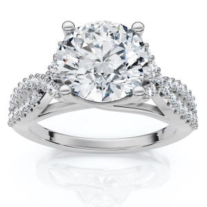 Puede incluir: Un anillo de tono plateado con una gran piedra central redonda de talla brillante sujeta por cuatro garras. La banda presenta un diseño de vástago dividido y retorcido, incrustado con pequeñas piedras redondas y transparentes a los lados.