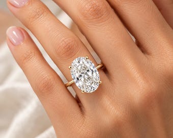 Könnte beinhalten: Ein goldener Ring mit einem großen, oval geschliffenen, klaren Edelstein, der von vier Krappen gehalten wird. Die Ringschiene besteht aus schlichtem, poliertem Gold und sorgt für ein klares Design, das den Glanz des Steins betont.