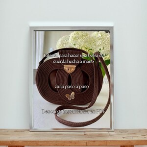 Op de afbeelding: Een bruine, handgemaakte touw tas met een cirkelvormig ontwerp en een gouden sluiting. De tas heeft een lange riem en een kleine vlinderbedel. Tekst op de afbeelding luidt "Tutorial voor het maken van een handgemaakte touw tas".