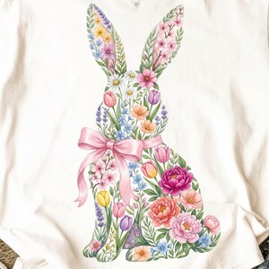 May include: A white t-shirt featuring a floral bunny design. The bunny is composed of various colorful flowers, including pink, yellow, and purple blooms, with a pink bow. The shirt has a classic crew neck and short sleeves.