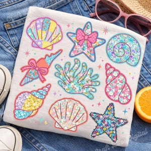 May include: White t-shirt featuring colorful seashell and starfish designs. The designs include floral patterns, bows, and a coral illustration. The shirt is on a denim background with sunglasses and a hat.