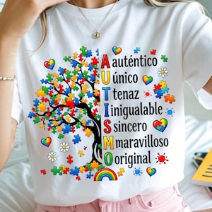 May include: White t-shirt featuring a colorful tree made of puzzle pieces. The word "AUTISMO" is written vertically in Spanish, with each letter representing a positive trait. Rainbows, hearts, and flowers decorate the design.