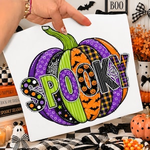 Könnte beinhalten: Ein quadratisches weißes Schild mit einer großen, stilisierten Kürbisillustration mit violetten, grünen und orangefarbenen Segmenten. Der Kürbis ist mit Mustern aus Spinnweben, Fledermäusen, Sternen und kleinen Kürbissen verziert. Das Wort SPOOKY ist in großen Buchstaben aufgedruckt.