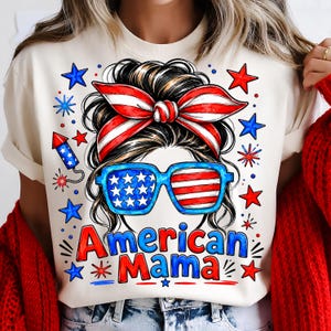 May include: A cream-colored t-shirt featuring a graphic of a messy bun hairstyle with a red, white, and blue striped headband, blue flag-patterned sunglasses, and the text American Mama, surrounded by red and blue stars and fireworks.