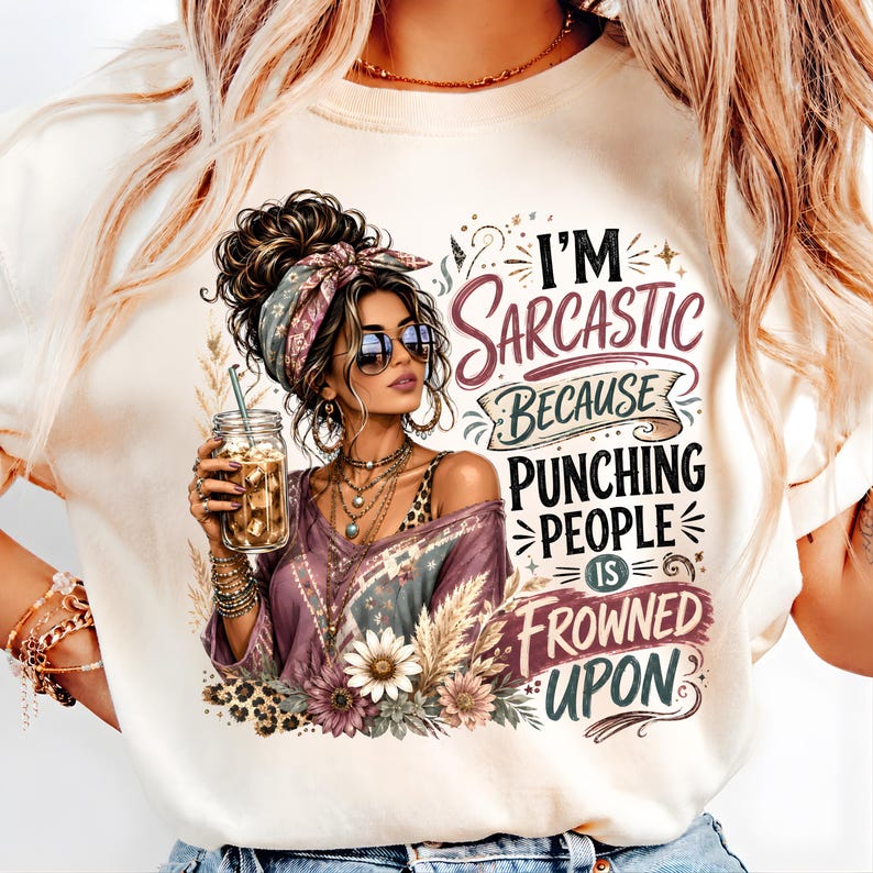 May include: A cream-colored t-shirt featuring a graphic of a person with a messy bun, sunglasses, and layered necklaces holding an iced coffee. The text reads, I'M SARCASTIC BECAUSE PUNCHING PEOPLE IS FROWNED UPON, surrounded by floral and leopard accents.