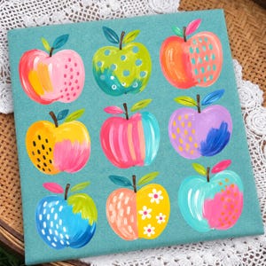 May include: A square teal canvas featuring a grid of nine stylized apples. Each apple displays unique patterns and colors, including pink, lime green, orange, yellow, purple, and blue, decorated with dots, stripes, dashes, and white flower motifs.
