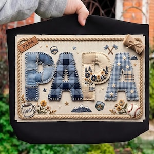 May include: Black tote bag featuring a decorative panel with the word "PAPA" in patchwork letters. The letters are in blue plaid and beige fabric, with embroidered details like mountains, flowers, and a baseball.