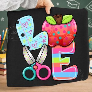 May include: A black pillow with a colorful design spelling "LOVE". The "L" is a blue heart with hearts and stars, the "O" is a red apple with green leaves, the "V" is a pair of scissors, and the "E" is striped.