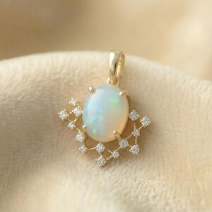 May include: A gold pendant featuring an oval opal gemstone with a shimmering, iridescent surface. The opal is surrounded by a delicate, openwork design of small diamonds. The pendant hangs from a gold bail, showcasing a piece of fine jewelry.