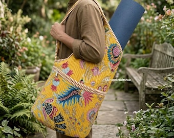 Puede incluir: Una bolsa acolchada amarilla para esterilla de yoga con un vibrante estampado floral y de cachemira en tonos azul, rosa y negro. La bolsa tiene una correa ancha para el hombro, un bolsillo frontal con cremallera y una esterilla azul oscuro.