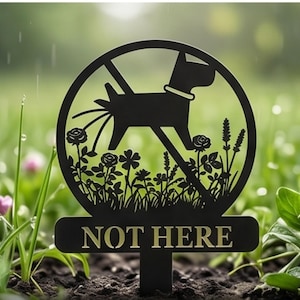 May include: Black metal garden stake with a silhouette of a dog inside a circle with a line through it, indicating "no". The stake has the words "NOT HERE" in gold lettering. The background is a green lawn with flowers.