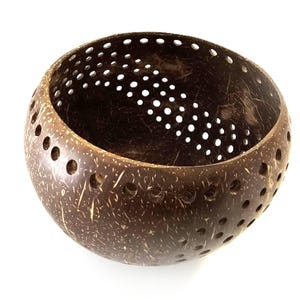 May include: A handcrafted, dark brown coconut bowl with a series of evenly spaced holes around the sides and top. The bowl has a natural, textured surface and is ideal for decorative purposes or as a unique serving dish.