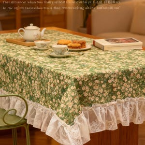 May include: A rectangular tablecloth with a green floral pattern and white lace trim. A tea set, cookies, and a book are on the table. A green metal chair is in the foreground. The text "Heat insulation and anti-slip" is visible.