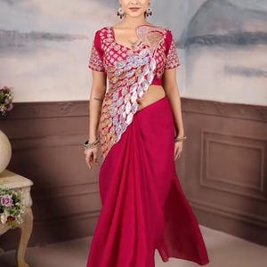 Puede incluir: Un sari magenta vibrante con una blusa a juego. La blusa presenta intrincados bordados y un adorno plateado y dorado. El sari está elegantemente drapeado, mostrando la tela fluida. La modelo lleva pendientes y pulseras.