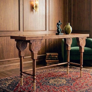 Puede incluir: Una consola de madera con detalles tallados y patas con puntas de latón. La mesa presenta una parte superior decorativa y está adornada con un jarrón verde y una escultura oscura. Se encuentra sobre una alfombra estampada, creando una estética elegante. La mesa mide unos 150 cm de largo.