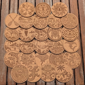 Peut inclure: Un ensemble de dessous de verre circulaires en liège avec des motifs gravés au laser, incluant des designs polynésiens, des fleurs tropicales, des créatures marines, des masques tiki, des palmiers, des pirogues et le texte MOANA, AHORA, MANA.