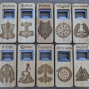 May include: Ten rectangular wooden bottle openers arranged in two rows. Each features a metal opener insert and laser-engraved Norse-themed designs and text, including Drakkar, Mjöllnir, Fenrir, Vegvisir, Huginn et Muninn, Viking, Yggdrasil, Jörmungandr, and Valknut.
