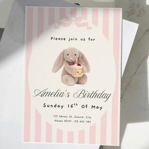 May include: A birthday invitation with a pink and white striped design. The invitation features a plush bunny holding a cupcake. Text reads "Please join us for Amelia's Birthday Sunday 16th of May".
