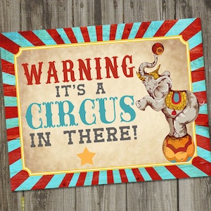 May include: A rectangular sign with a circus theme. The sign features the text "WARNING IT'S A CIRCUS IN THERE!" in red and teal lettering. An illustration of an elephant balancing on a ball is on the right side of the sign.