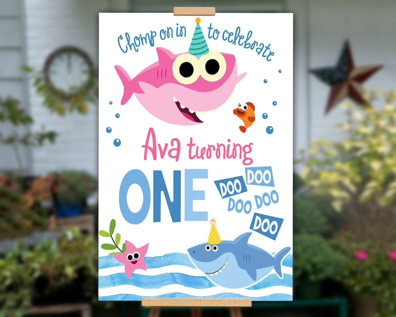 K&ouml;nnte beinhalten: Ein wei&szlig;es Schild mit einem blauen und rosa Cartoon-Hai mit dem Text "Chomp on in to celebrate Ava turning ONE doo doo doo doo doo doo". Das Schild hat einen blauen und wei&szlig;en Aquarellhintergrund mit einem Seestern und Seegras.
