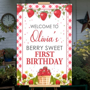 May include: A welcome sign for Olivia's first birthday, featuring a strawberry theme. The sign has a red and white gingham border, with strawberries and flowers at the top and a basket of strawberries at the bottom. Text reads "Welcome to Olivia's Berry Sweet First Birthday."
