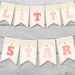 May include: A banner with the words "LITTLE STAR" in pink letters. The banner is made of cream-colored pennants with pink and white striped borders. Gold glitter and star accents decorate the top of each pennant. The banner is strung on a gold cord.