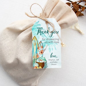 Puede incluir: Una bolsa de regalo con una etiqueta que presenta tablas de surf, palmeras y el texto "Thank you for showering us with love". La etiqueta est&aacute; atada con hilo. La bolsa es de tela beige claro.