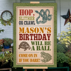 May include: A green, brown, and orange birthday party sign with a snake, turtle, and frog. The sign reads "Hop, Slither or Crawl Mason's Birthday Will Be A Ball Come On In If You Dare!"