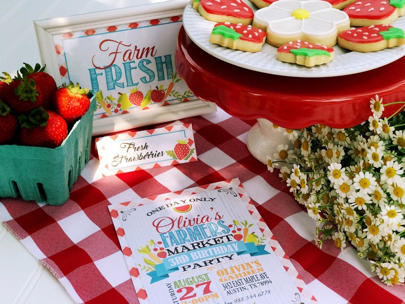 Puede incluir: Una exhibici&oacute;n con tem&aacute;tica de mercado de agricultores con fresas frescas, galletas y un letrero que dice "Farm Fresh". Un mantel a cuadros rojos y blancos prepara el escenario para una invitaci&oacute;n de cumplea&ntilde;os. Las galletas est&aacute;n decoradas para parecer fresas.