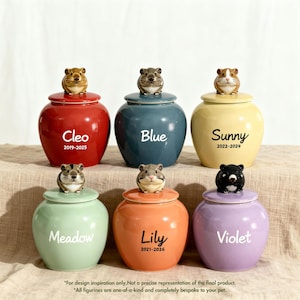 Peut inclure: Six pots en céramique avec couvercles, chacun surmonté d'une petite figurine de cochon d'Inde sculptée. Les pots sont rouges, bleus, jaunes, vert clair, orange et violets, avec des noms et dates imprimés comme Cleo, Blue, Sunny, Meadow, Lily et Violet.