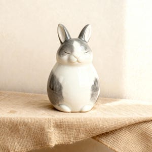 Custom grey ceramic rabbit urn for ashes, handcrafted bunny memorial pottery keepsake. Minimalist design inspired by gentle rabbits resting on soft hay, symbolizing serenity and love. Handmade pet urn, personalized with name or motif, perfect for rabbit lovers and pet owners seeking elegant, modern remembrance. Ideal ashes container, pottery urn with smooth matte finish, durable and timeless bunny memorial art.