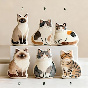 Puede incluir: Seis figuras de cerámica de gatos en varias poses y colores. Los gatos están pintados con detalles, incluyendo patrones siameses, calicó y atigrados. Cada gato tiene un diseño único, algunos sentados y otros de pie.