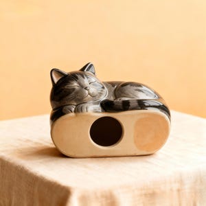 A unique pottery curled up cat urn created in a realistic yet artistic sleeping form, designed for cat cremation ashes up to 13.5kg or 30lb. Fully customised from your photos to capture markings and character. This handmade ceramic pet memorial offers a secure bottom plug and a calming curled silhouette. Ideal for personalised cat urn buyers, pet loss gifts, and those seeking an artistic feline remembrance sculpture.