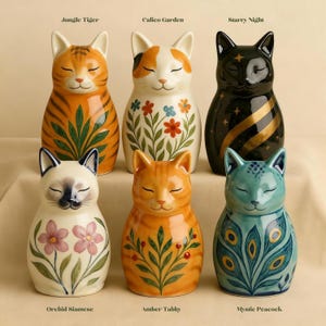 May include: Six ceramic cat figurines with closed eyes, each with unique designs. The "Jungle Tiger" has orange and black stripes, while "Calico Garden" features floral patterns. "Starry Night" is black with gold stripes. "Orchid Siamese", "Amber Tabby", and "Mystic Peacock" are also shown.