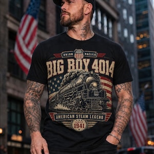 Puede incluir: Una camiseta negra con un gráfico de la locomotora de vapor Union Pacific Big Boy 4014. El diseño incluye el texto "BIG BOY 4014", "UNION PACIFIC", "AMERICAN STEAM LEGEND" y "SINCE 1941" sobre un fondo de bandera estadounidense desgastada.