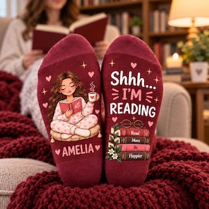 May include: A pair of maroon socks featuring a graphic of a person reading a book while holding a mug, the name AMELIA, and the text Shhh... I'M READING above a stack of books with the words Read More Be Happier and small heart accents.