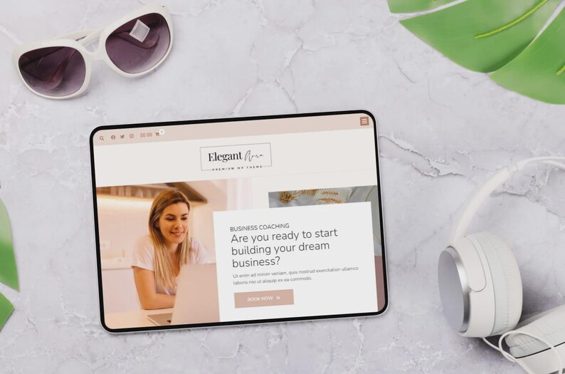Op de afbeelding: Een digitale tablet toont een website met de tekst "Elegant Aria" en "Premium of Icons". Het scherm toont een vrouw die op een laptop werkt. Witte zonnebril en koptelefoon zijn ook zichtbaar.