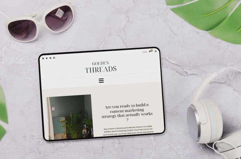 Puede incluir: Una tableta digital que muestra el sitio web "GOLDEN THREADS", con el texto "Are you ready to build a content marketing strategy that actually works?". Tambi&eacute;n se ven gafas de sol y auriculares blancos.