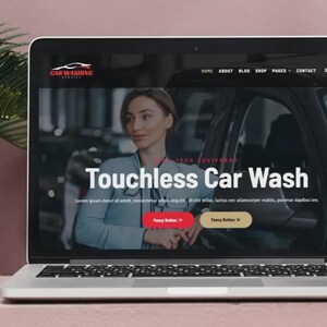 K&ouml;nnte beinhalten: Ein Laptop zeigt eine Website f&uuml;r eine Autowaschanlage. Der Bildschirm zeigt eine Frau in einem blauen Hemd mit dem Text "Touchless Car Wash". Die Website hat eine rote und eine goldene Schaltfl&auml;che. Der Laptop steht auf einer rosa Oberfl&auml;che.